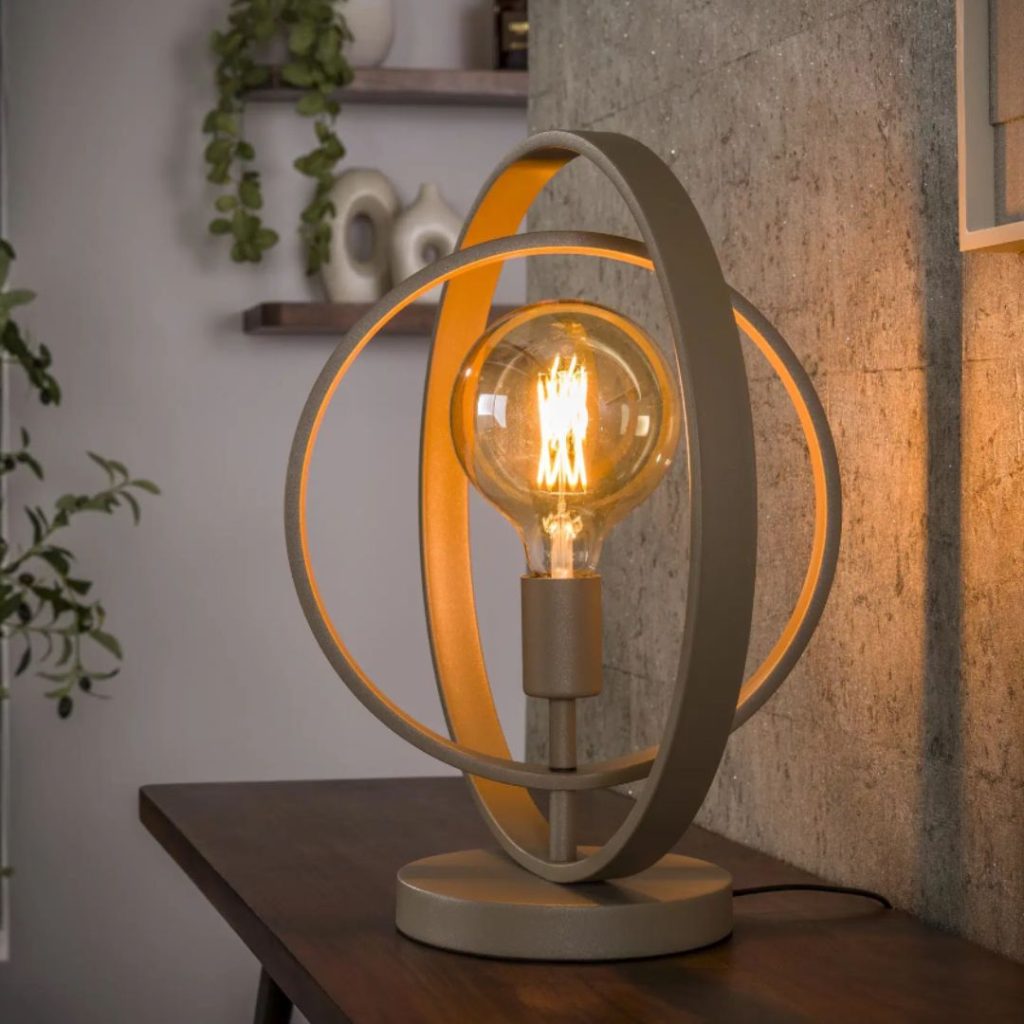 Tafellamp Roxy in beige met draaibare metalen ringen, brandend op een dressoir in een sfeervol interieur.