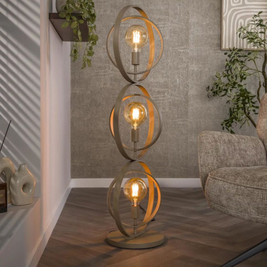 beige vloerlamp met draaibare metalen ringen die brandend naast een stoel staat in een warm ingericht interieur.