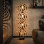 Vloerlamp met metalen ringen naast een bank in een rustig interieur terwijl de lamp aan staat.