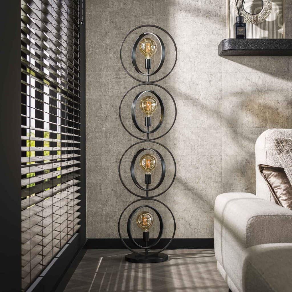 Vloerlamp met metalen ringen naast een bank in een rustig interieur terwijl de lamp uit staat.